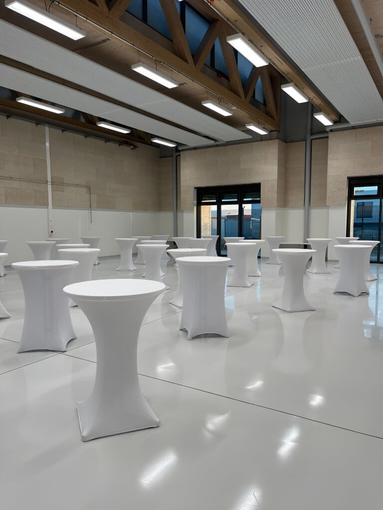 Heller, moderner Raum mit hohen Decken und Stehtischen, die elegant mit Stehtischhussen Deluxe für eine Veranstaltung eingedeckt sind