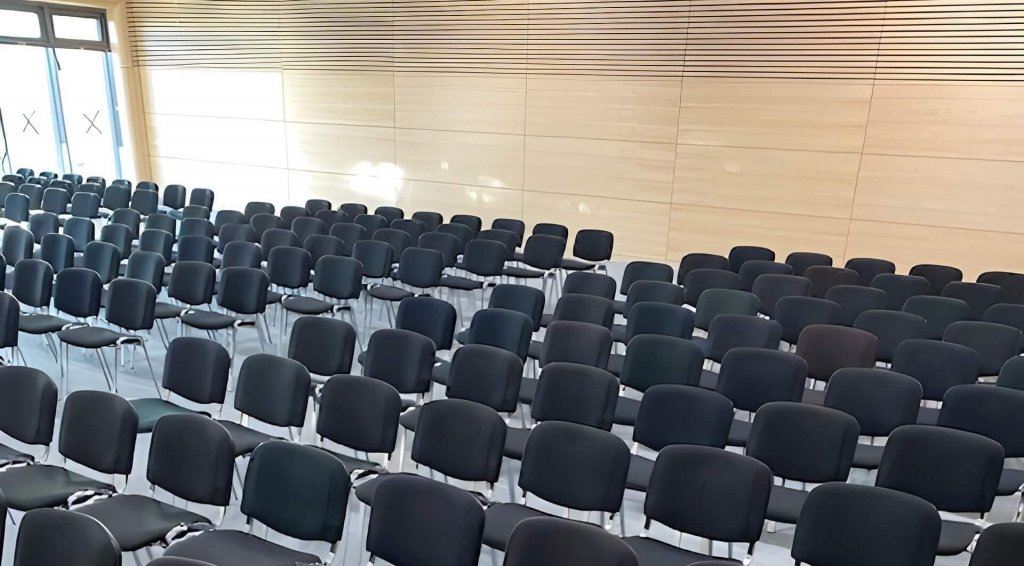 Reihen leerer schwarzer Stühle stehen ordentlich in einem modernen, hellen Raum mit Holzwänden und großen Fenstern